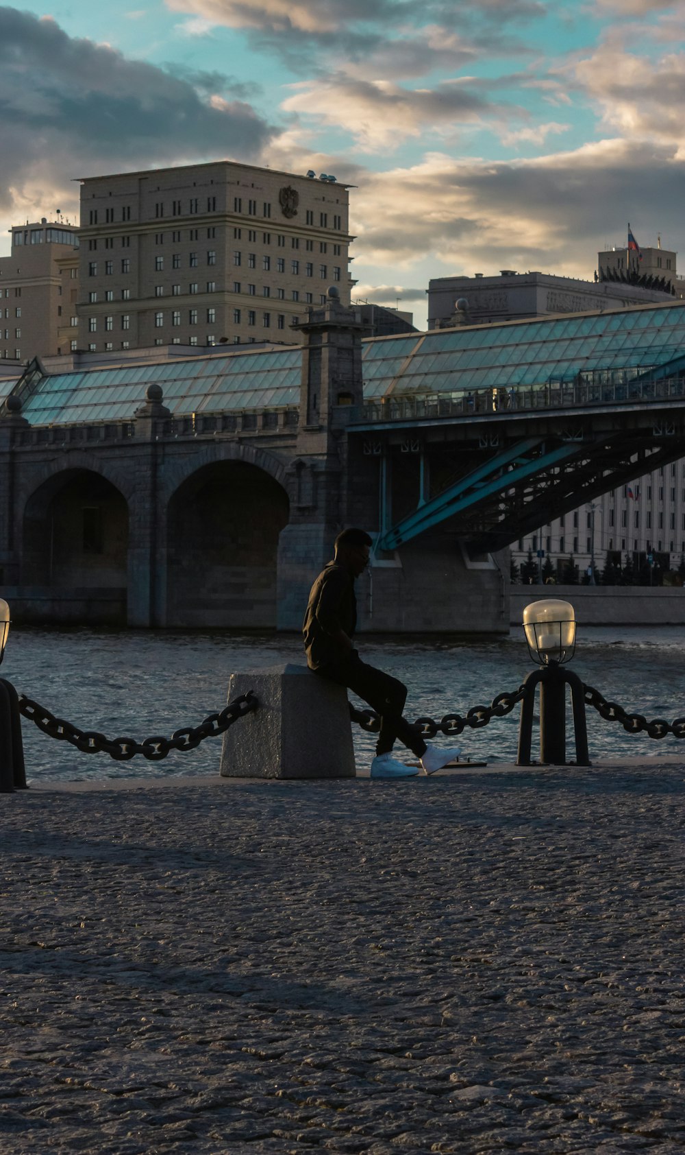 man sitting on concrete post beside bridge during daytime