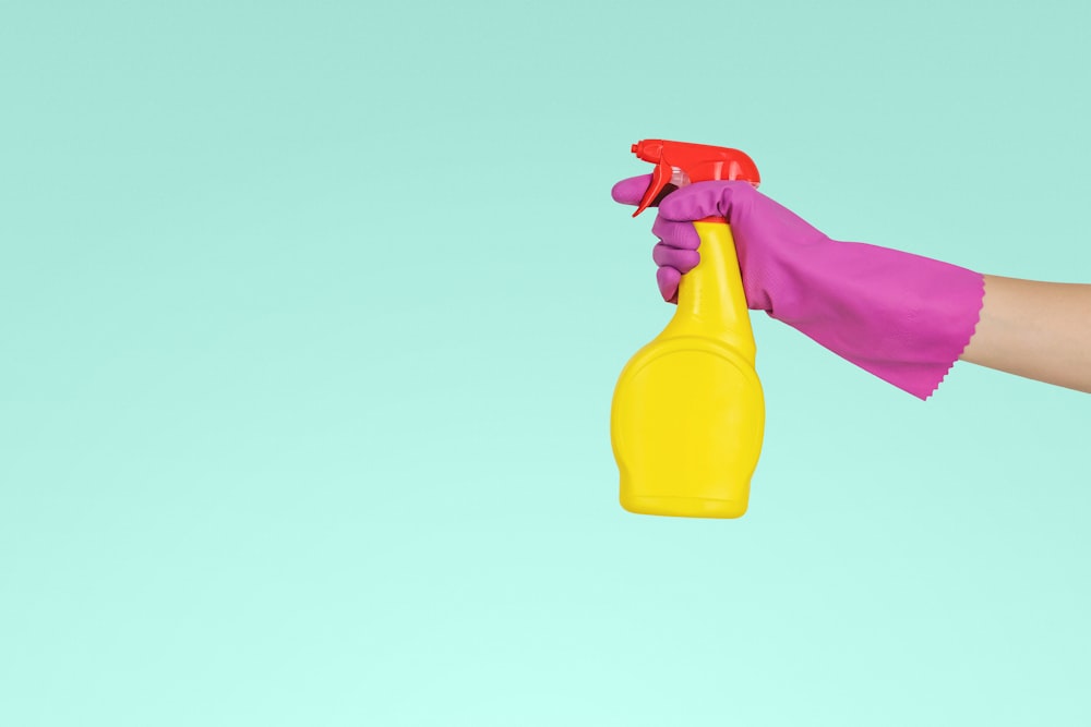 Persona che tiene in mano un flacone spray di plastica gialla