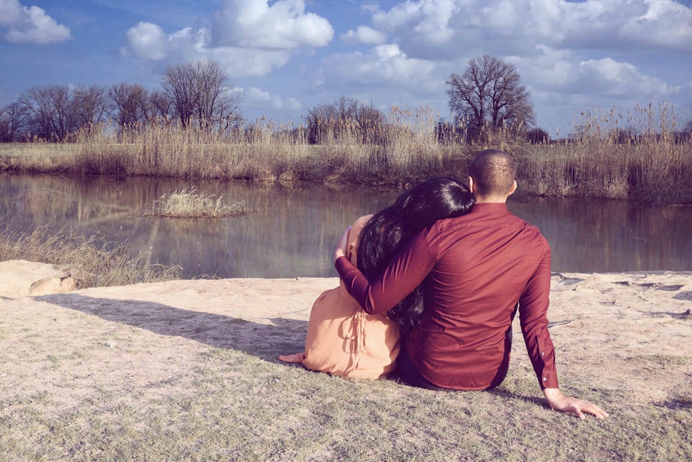 sitting man and woman overlooking at calm body of water during daytime