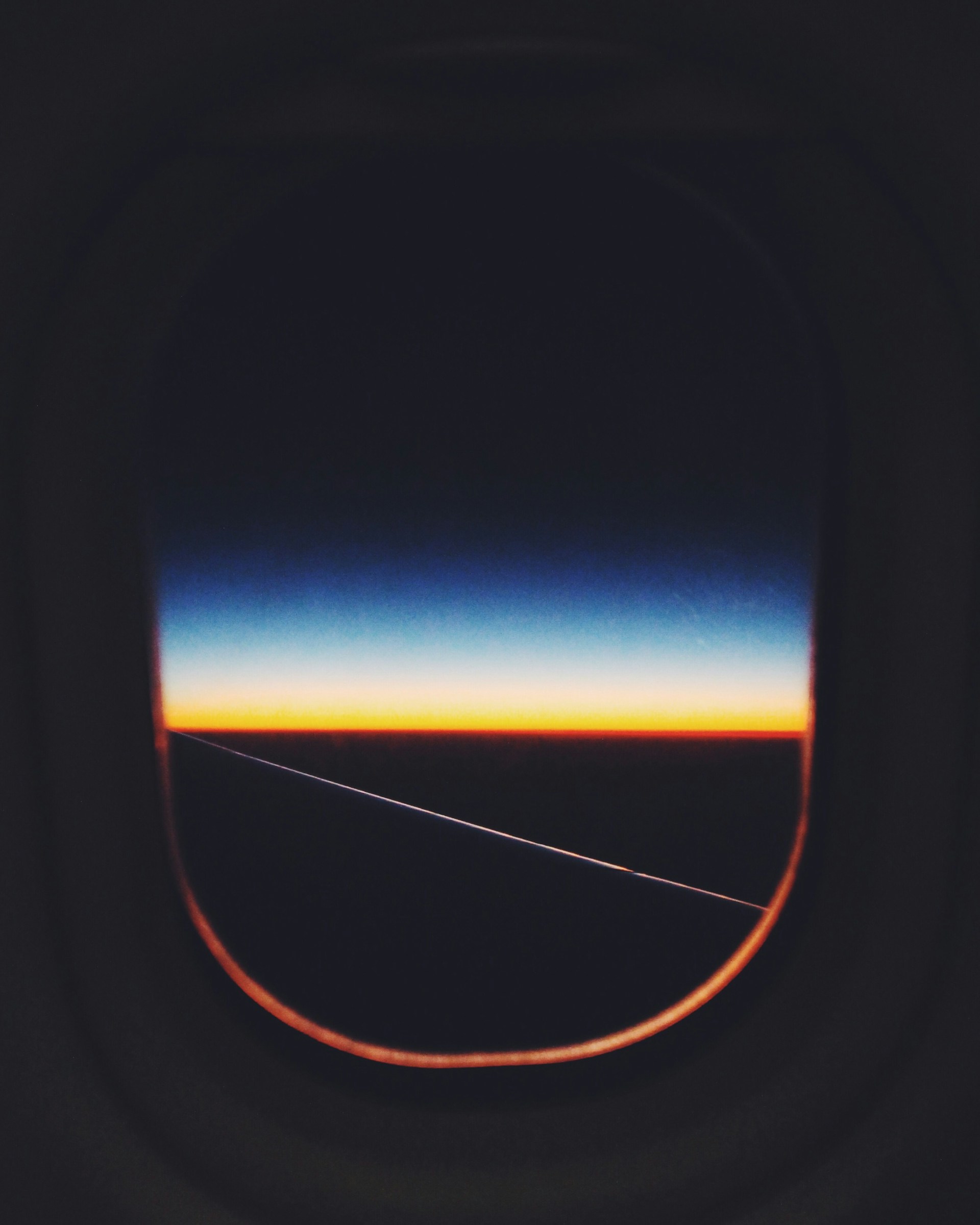 A view of a horizon seen from an airplane window, showcasing a stunning gradient of colors transitioning from deep blue to orange as the day turns to night.