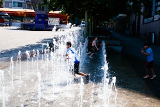 Children laughing as they splash in a colorful shallow pool with fountains.