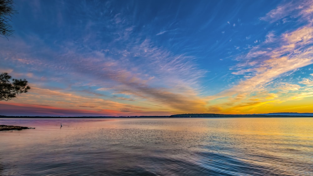 a beautiful sunset over a lake with clouds in the sky