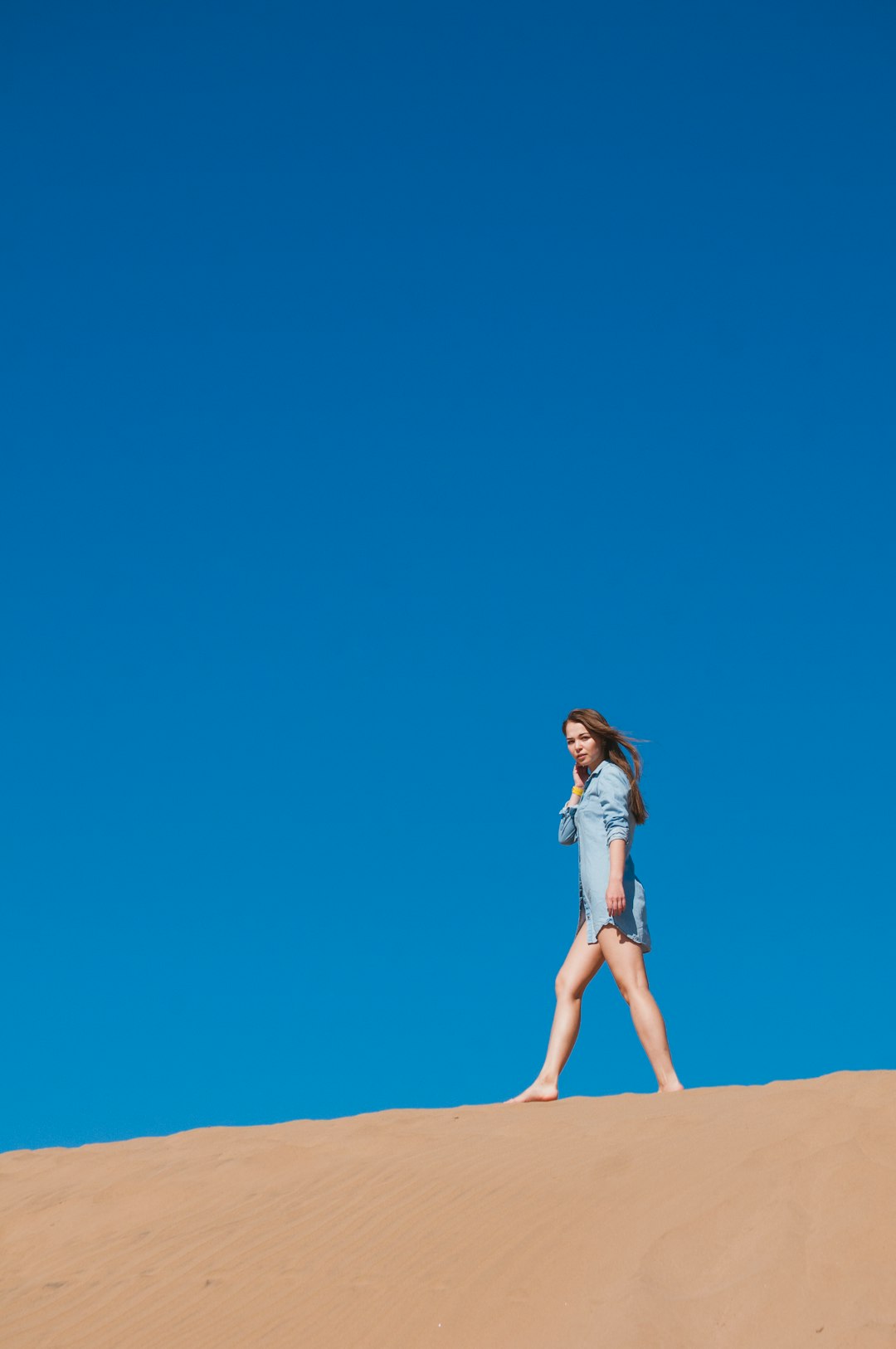 woman wearing blue denim jacket walking on dune sand