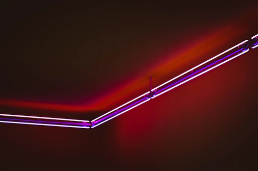 Finished neon sign glowing in vivid pink and purple hues on a dark wall.
