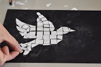 Close-up of hands carefully arranging collage elements on canvas.