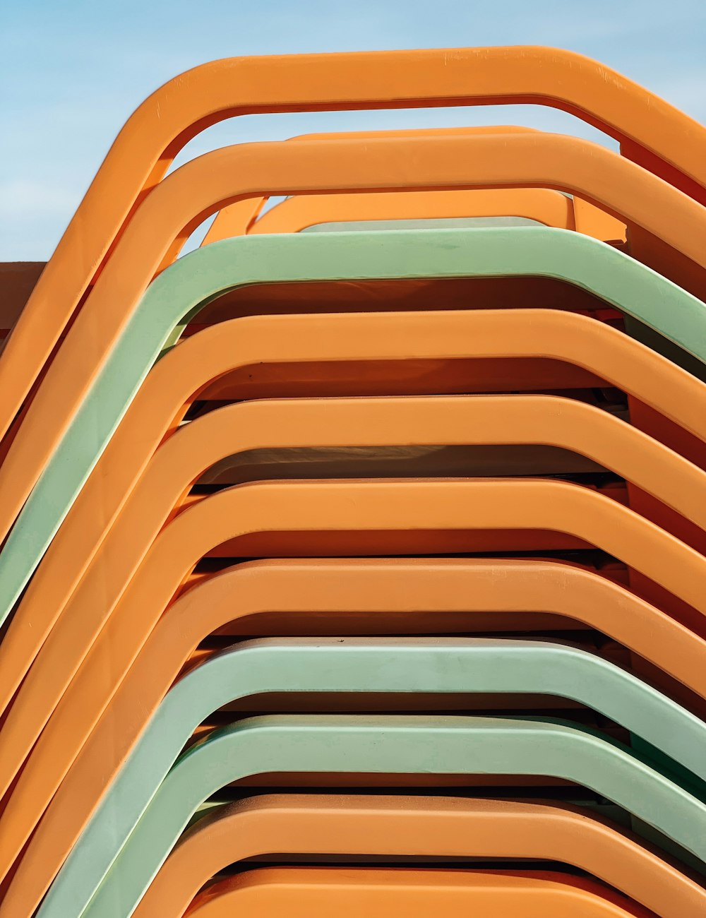 a stack of orange and green chairs against a blue sky