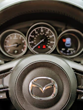 Close-up of a Mazda steering wheel with dashboard lit up during a test drive.