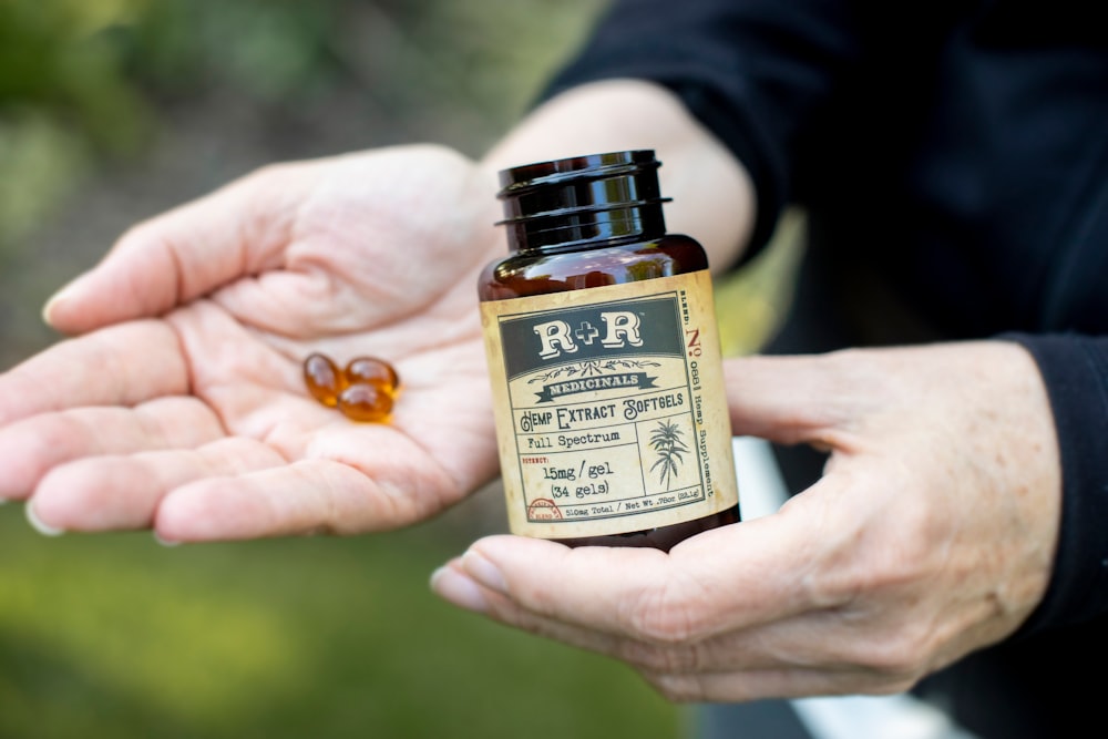person holding R+R bottle and 3 gel capsules