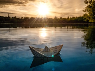 A whimsical scene of a child sailing a paper boat on a glowing moonlit lake.