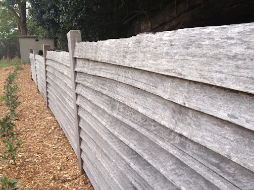 A team member planting shrubs near a newly built wooden fence.