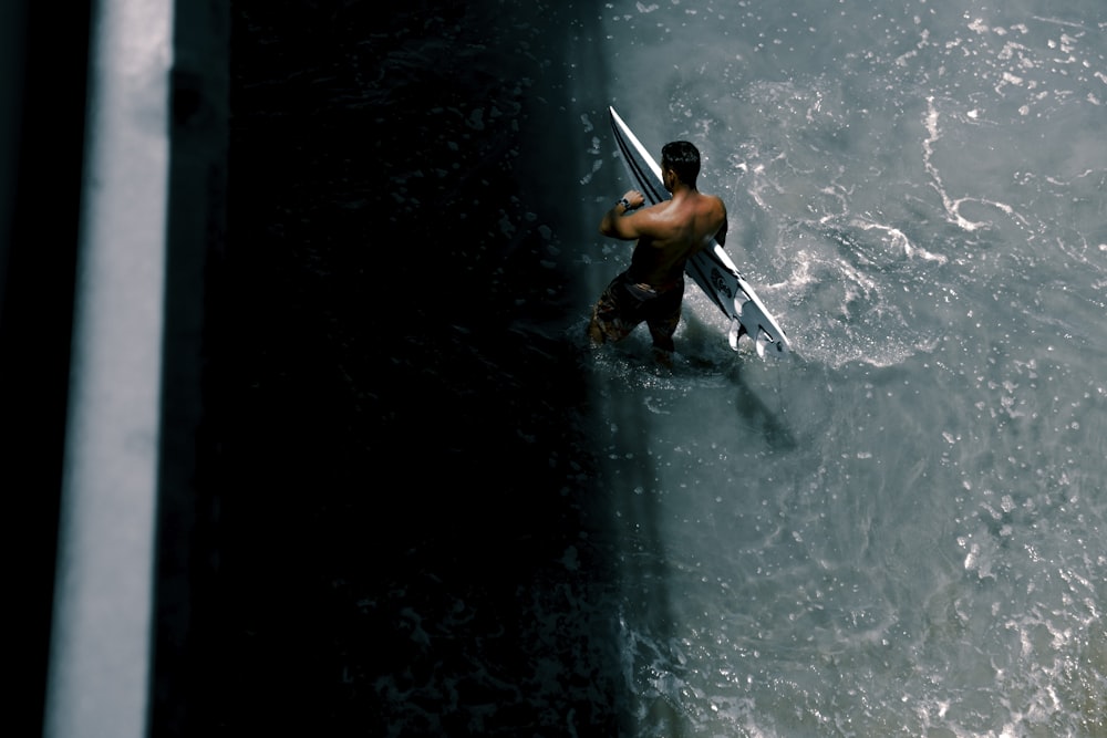 high-angle photography of man carrying white surfboard