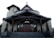 A church building with a large wooden door and steep staircase. The structure features a cross on the roof peak, arched windows, and is flanked by potted plants. The exterior walls are a light beige color, contrasting with the dark wooden trimmings of the roof and support beams.