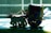 A decorative wooden toy depicting a bullock cart with intricate designs. The cart has a colorful, patterned canopy and is being pulled by a carved bull figure. The scene is backlit, creating strong contrast and shadows on the surface.