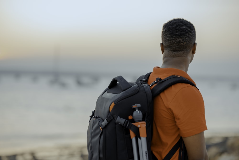 man wearing orange shirt holding black backpack close-up photography