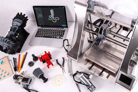 a laptop computer sitting on top of a table near 3d printers and manufacturing tools