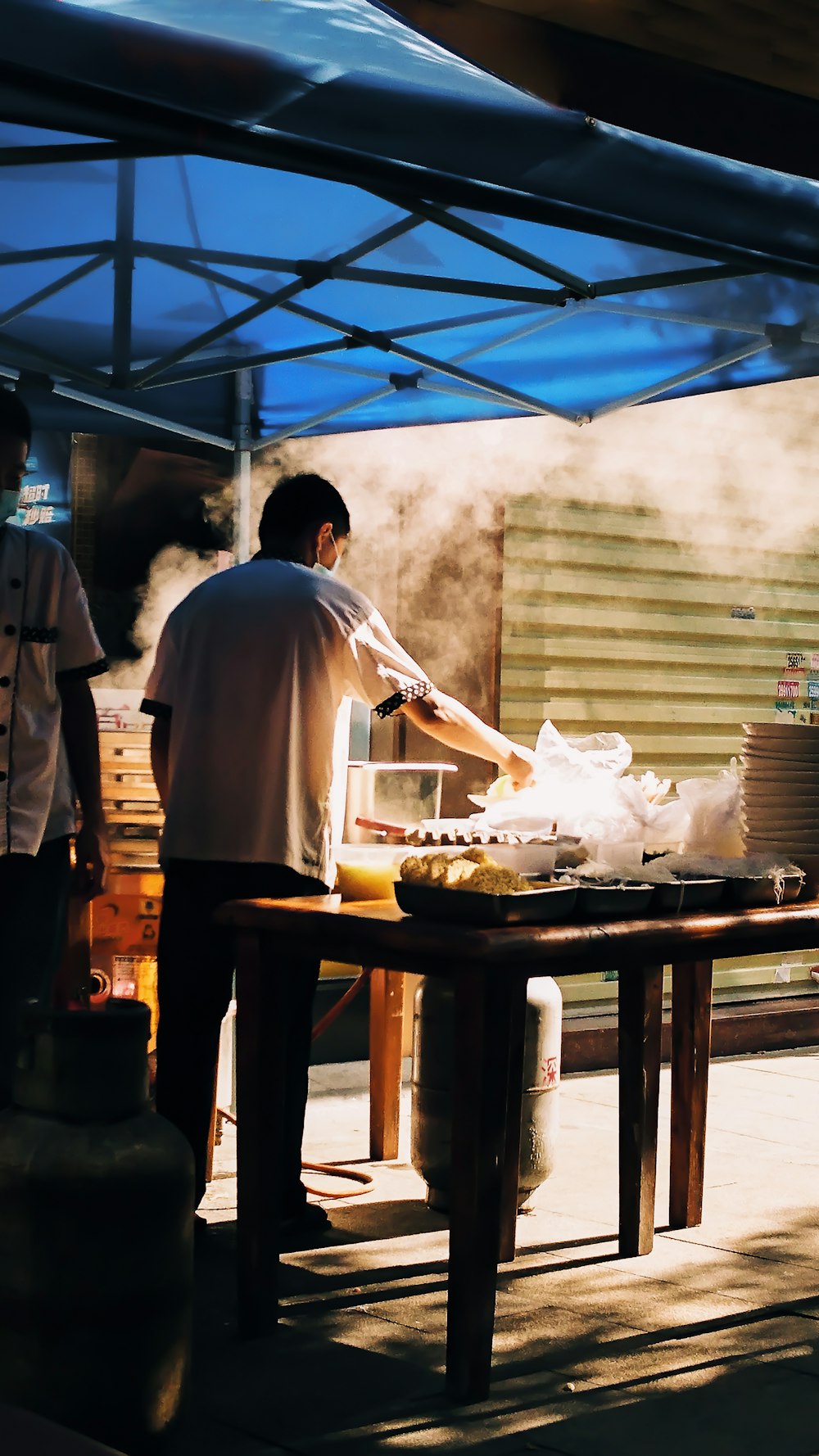 man barbecuing under blue canopy