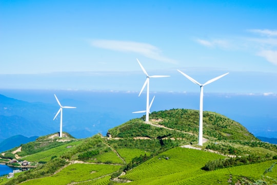 Wind turbines spinning on green hills under a bright blue sky in rural Galicia.