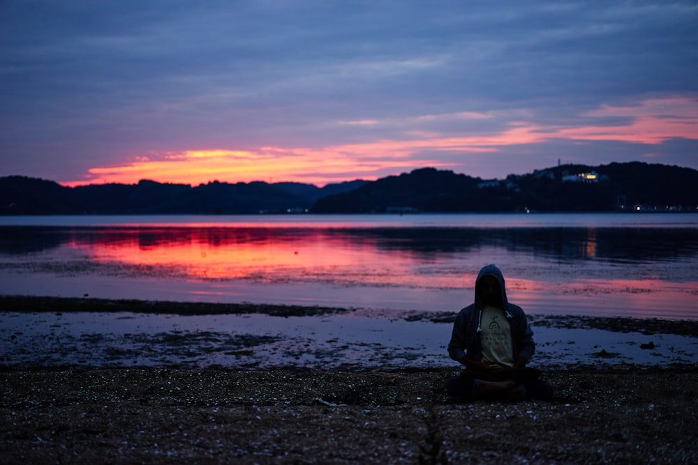 homme assis en position de lotus sur la plage au coucher du soleil