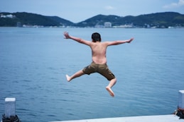 kid jumping from a dock to body of water during daytime