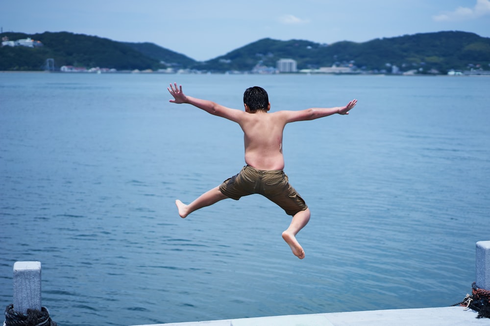kid jumping from a dock to body of water during daytime