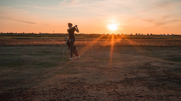 A close-up of a golfer's swing at sunset on the course.