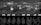A series of industrial pressure gauges are mounted on a brick wall. Below them are several metal valves with handles, possibly part of an old machinery system. The image is in black and white, adding a vintage or historical feel.