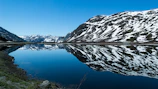 Snow-capped mountains reflected perfectly in a crystal-clear alpine lake under a blue sky.