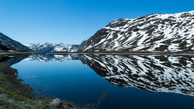 Snow-capped mountains reflected perfectly in a crystal-clear alpine lake under a blue sky.
