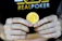 A person holds a golden coin with a Bitcoin symbol between their fingers. The background features the word 'REALPOKER' in bold letters on a dark shirt.