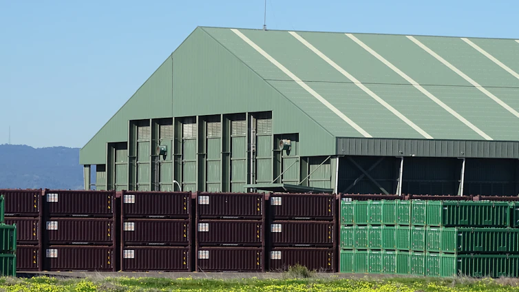 A serene warehouse surrounded by lush greenery, with solar panels on the roof and delivery trucks featuring green leaf logos.