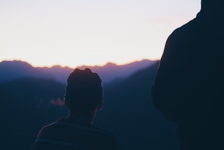 Sunset view from a mountain peak with silhouettes of two travelers
