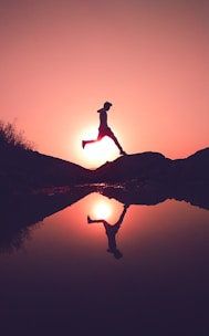 man jumping on rock beside lake