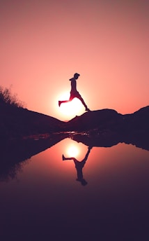 man jumping on rock beside lake