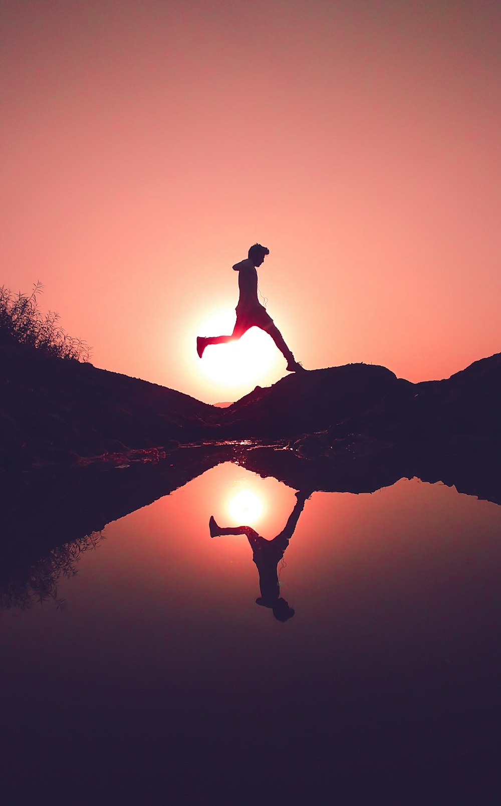 Mann springt auf Felsen neben See