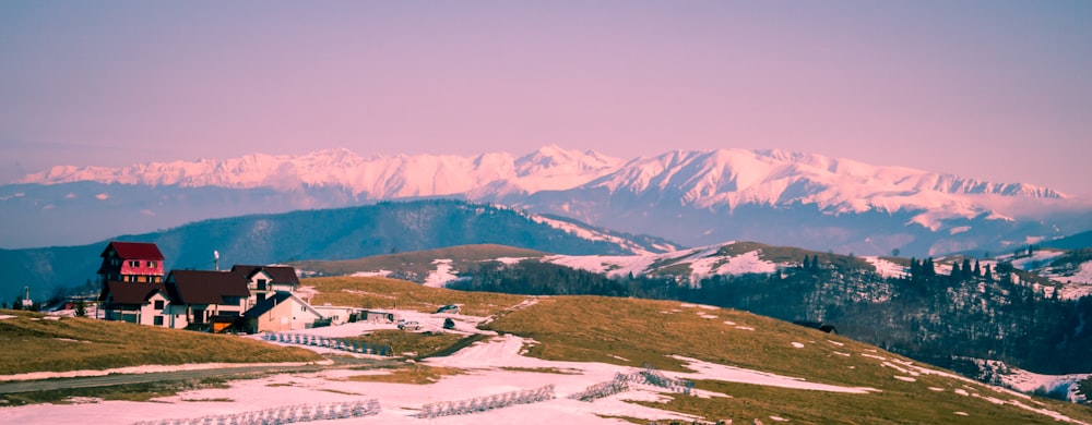 a house on top of a snowy hill with mountains in the background