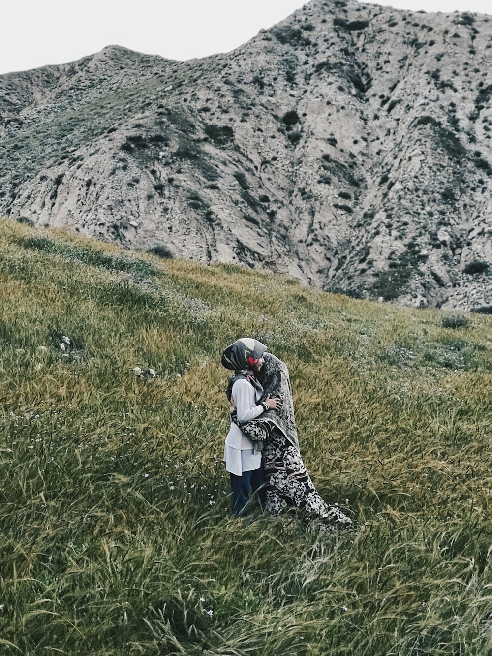 two person standing and hugging in green field beside mountain