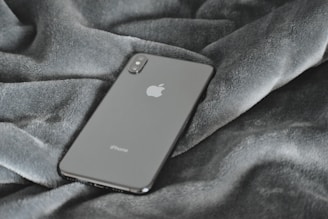 A sleek smartphone rests on a textured grey fabric surface, showcasing its minimalist design and glossy finish.