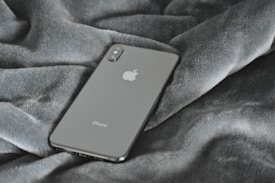 A sleek smartphone rests on a textured grey fabric surface, showcasing its minimalist design and glossy finish.