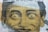 A large, artistic depiction of a person's face with exaggerated features, notably wide and expressive eyes and a playful smile. The image appears to be created as part of a mural or street art piece, with a grid overlay strategy giving it an urban and textured appearance.