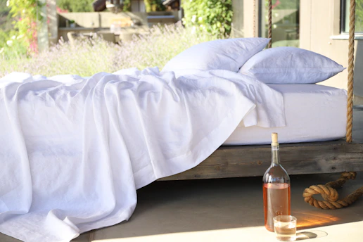 two white pillows on bed and glass of bottle near drinking glass on floor