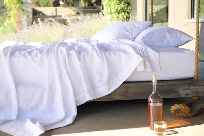 two white pillows on bed and glass of bottle near drinking glass on floor