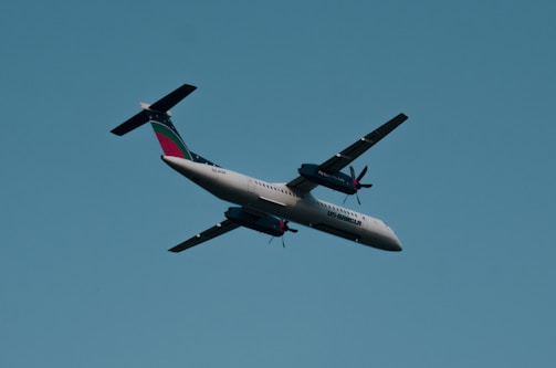A propeller-driven airplane with a distinctive tail design flies across a clear blue sky. The plane has two engines mounted on the wings.