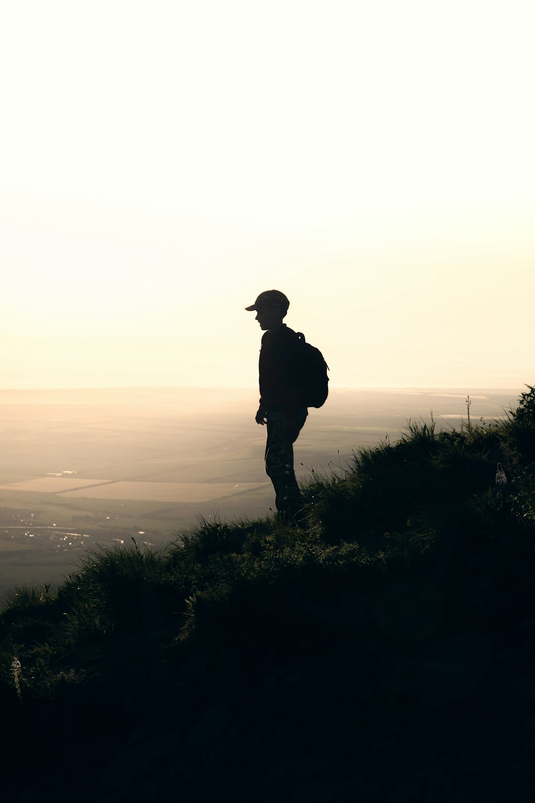 silhouette of man with backpack standing on slope of hill at dusk