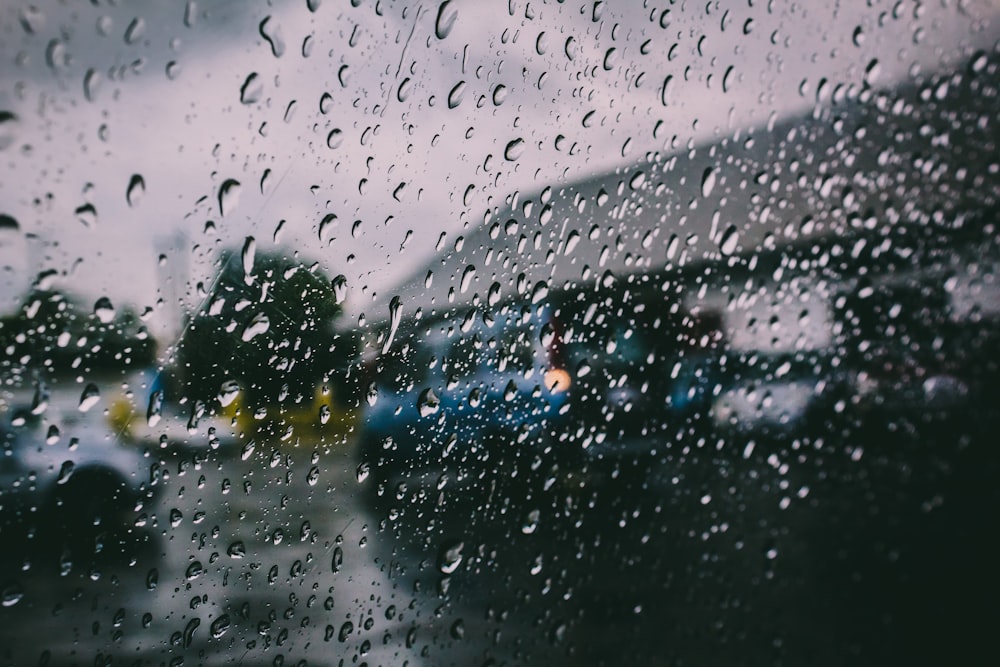 a rain covered window with cars parked in the background