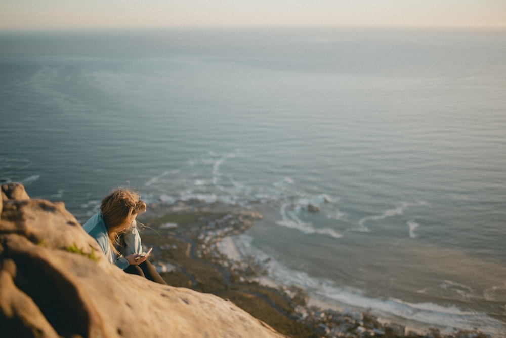 회색 셔츠를 입고 바다 근처 절벽에 앉아 있는 여자