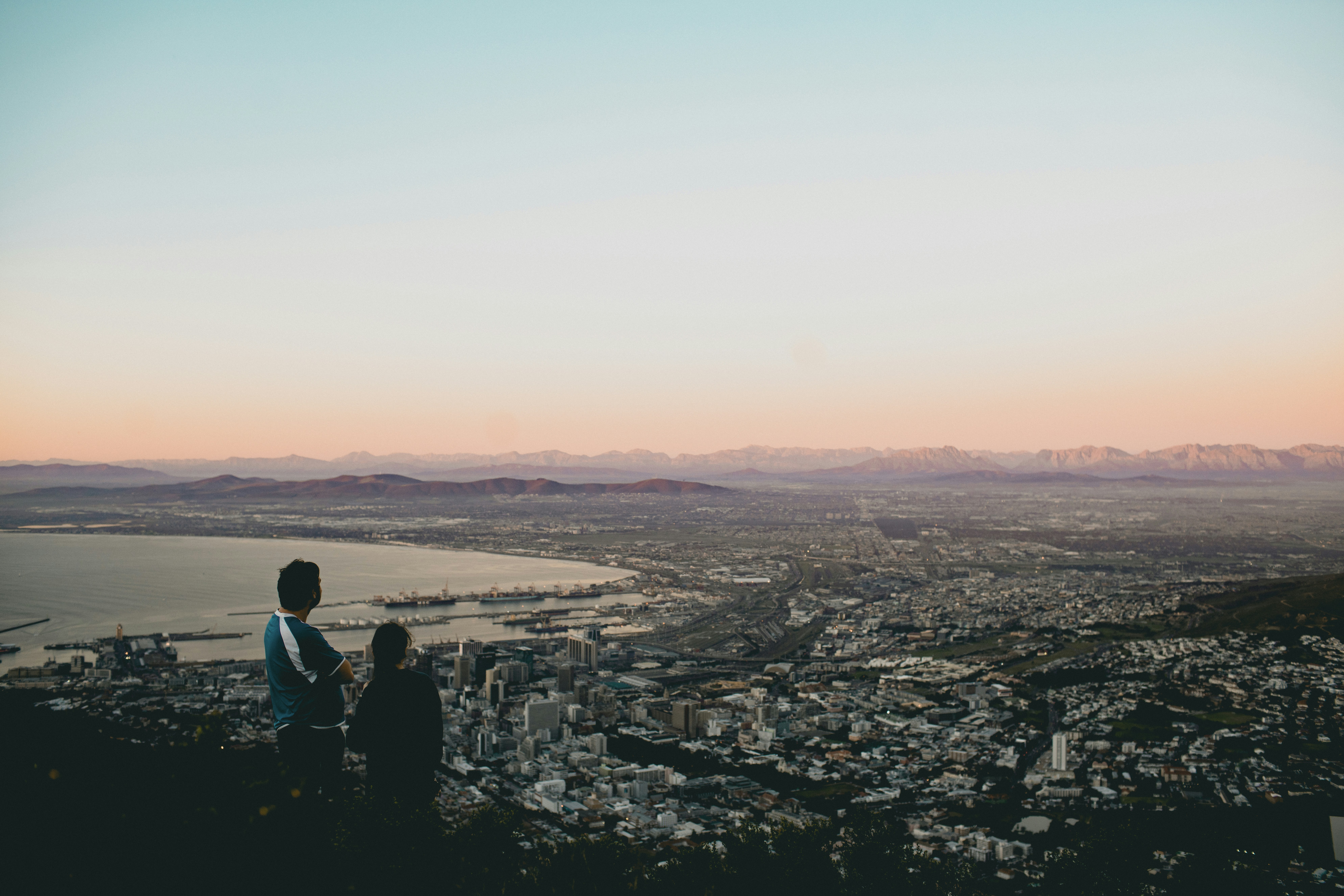 two people standing on top of a hill overlooking a city
