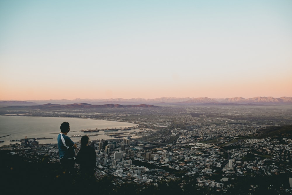 two people standing on top of a hill overlooking a city