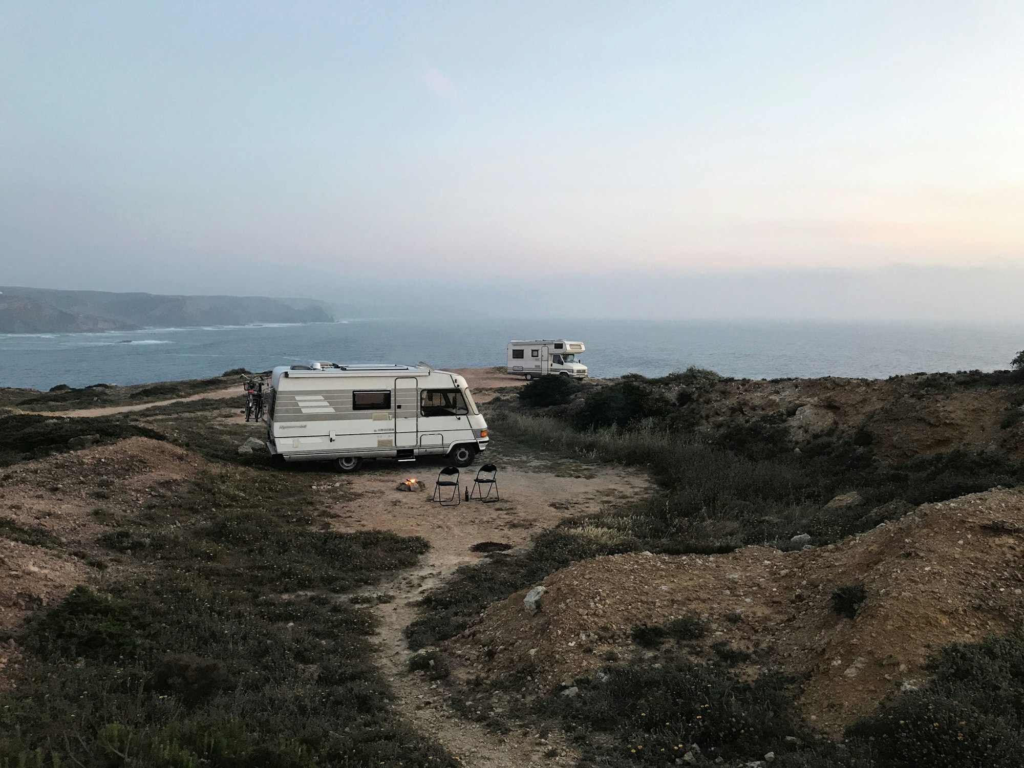 vanlife situation in portugal, campervans parking by the coast, having a camp fire and enjoying the sunset (amado beach, portugal)