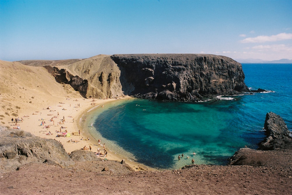 a sandy beach with clear blue water next to a cliff