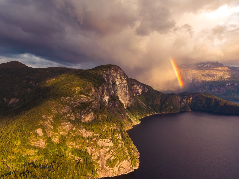 body of water near mountain with rainbow during daytime